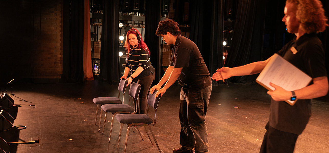 3 SCS staff on stage setting up the performance